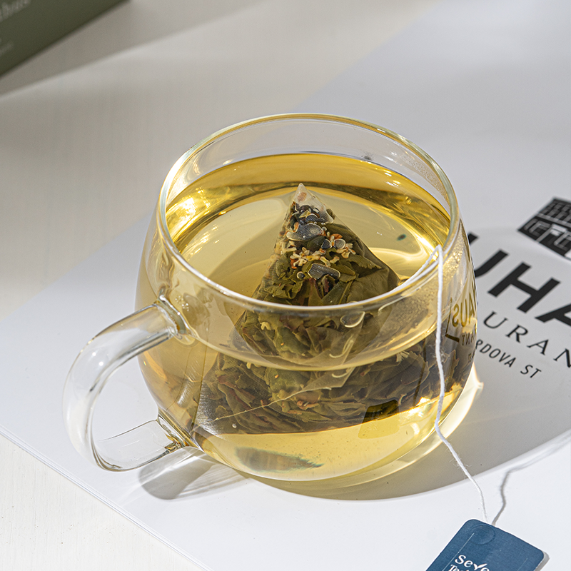 A glass cup of brewed osmanthus oolong tea with a pyramid tea bag