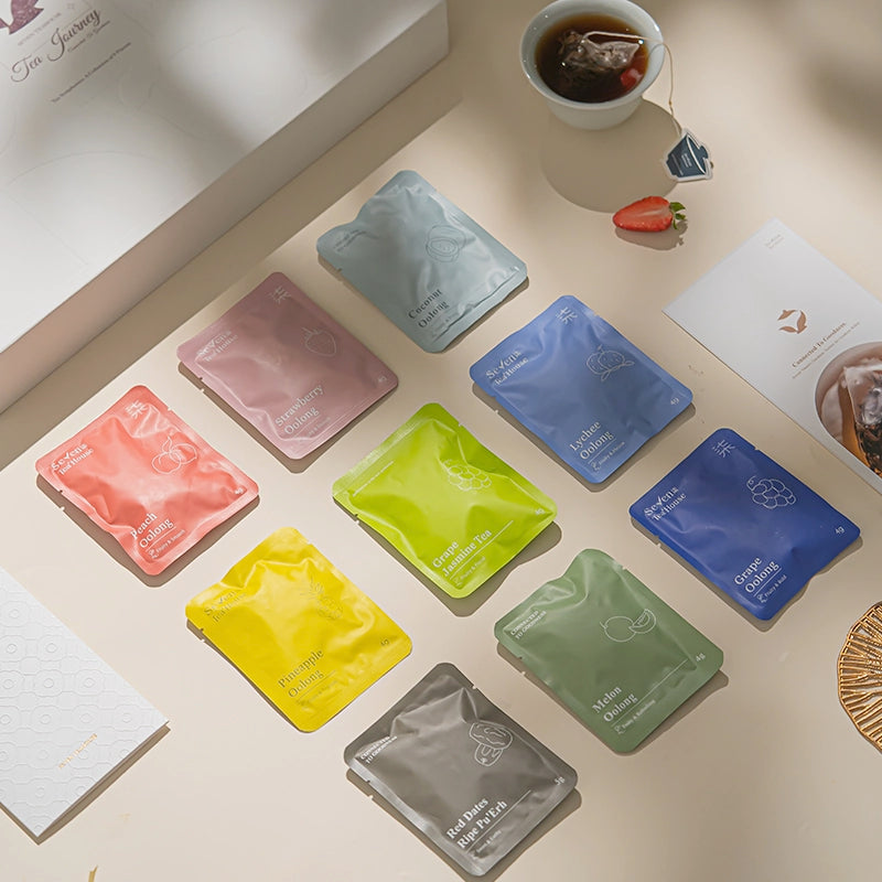 Assorted colorful tea bags on a light surface with a cup of tea and half a strawberry