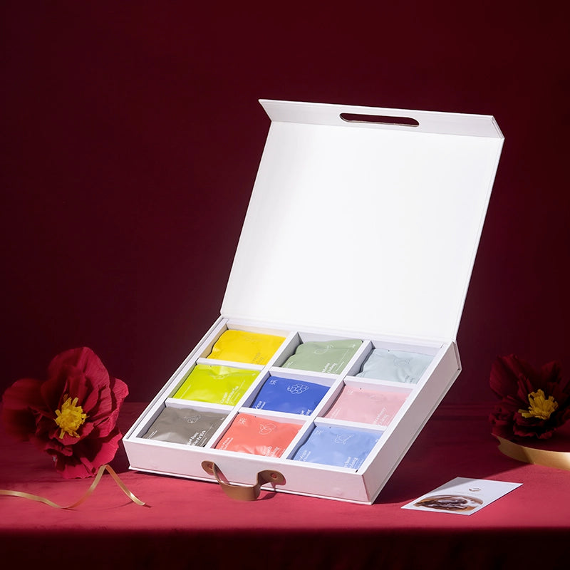 Open white box with colorful tea bags on a red surface with flowers